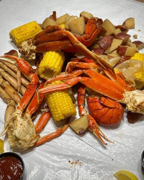A seafood boil with crab legs, lobster tail, corn on the cob, and red potatoes served on white paper with dipping sauce.