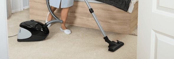 A woman is cleaning the carpet with a vacuum cleaner