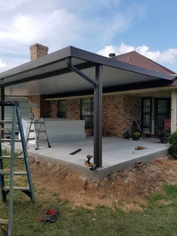 A patio cover is being installed on the back of a brick house.