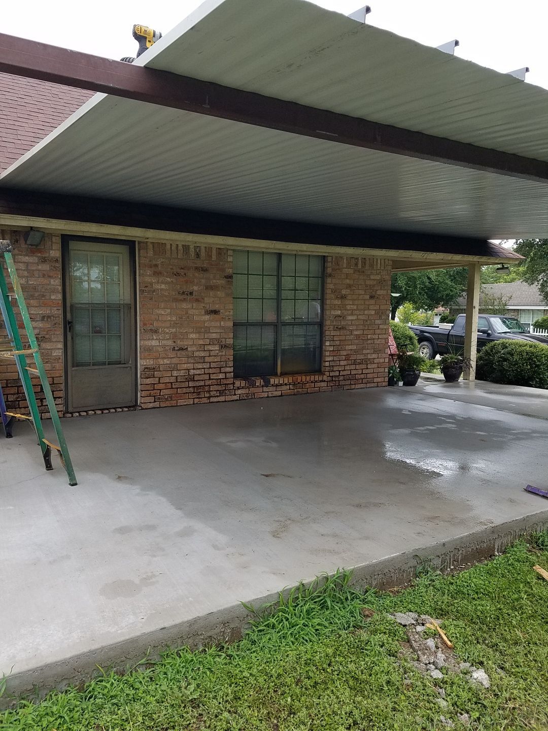 A brick house with a covered porch and a ladder in front of it.