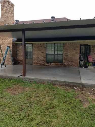 A covered patio with a ladder in front of a brick house.