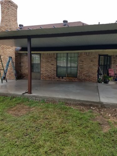 A covered patio with a ladder in front of a brick house.