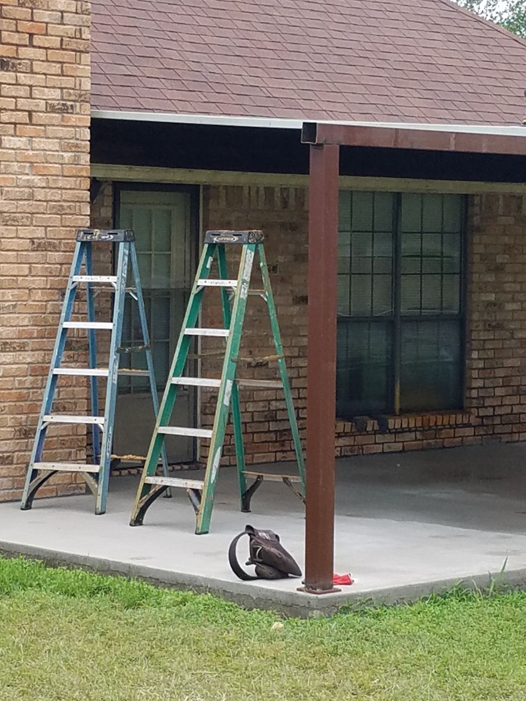 Two ladders are sitting on a patio in front of a brick house.