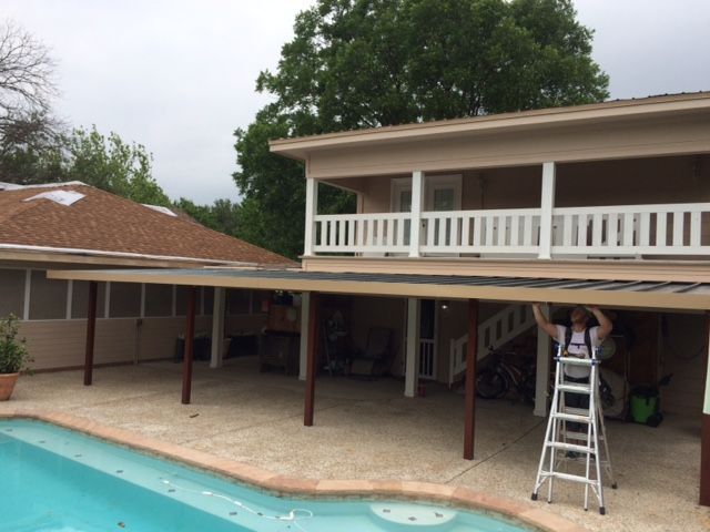 A man standing on a ladder in front of a house next to a pool