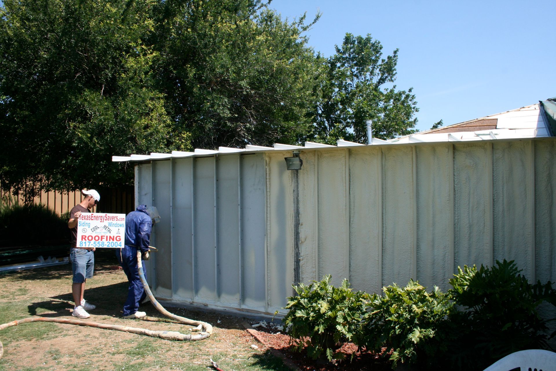 A man spraying foam on a fence while holding a sign