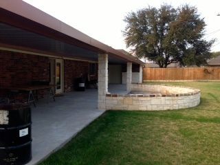 A patio with a barrel in front of it and a tree in the background.