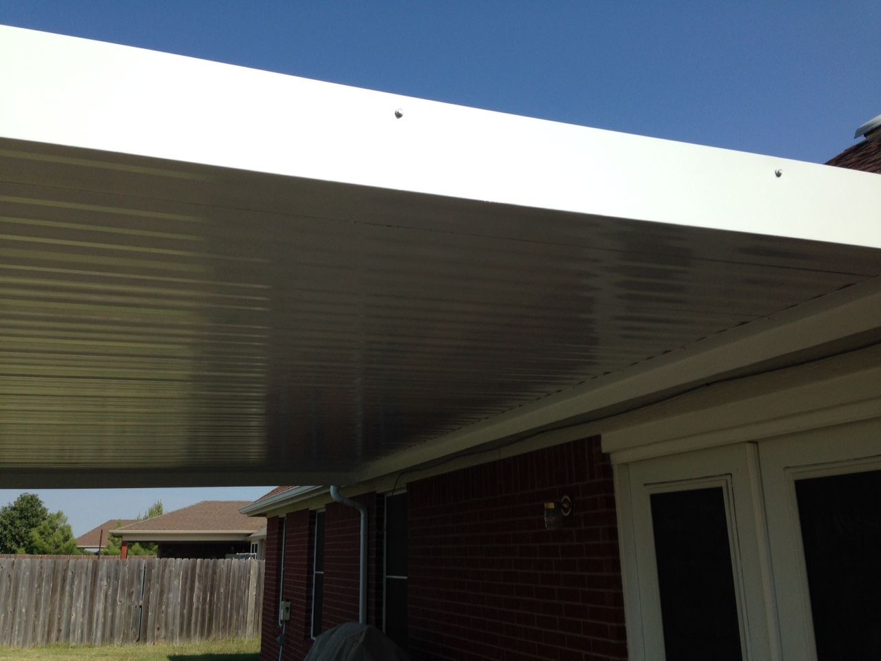 A white carport is attached to the side of a brick house.