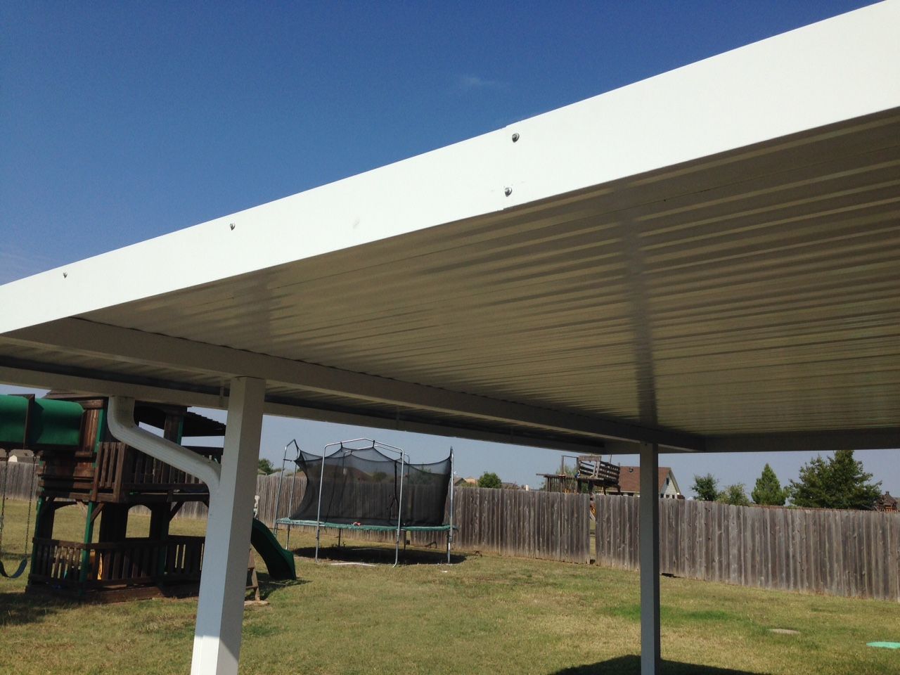 A white carport in a backyard with a playground in the background