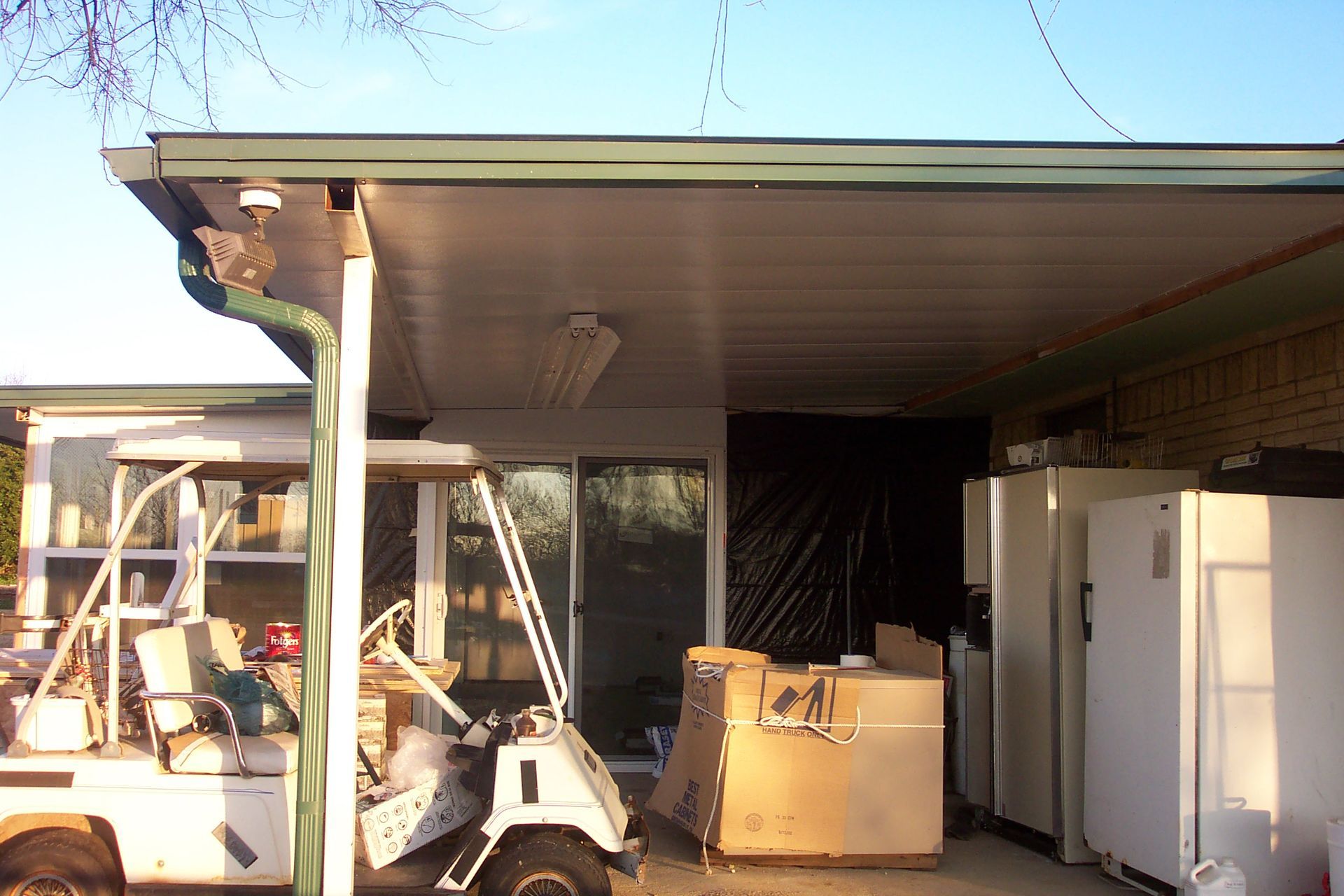 A golf cart is parked under a covered porch in front of a house.