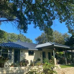 A white house with a metal roof and a porch surrounded by trees
