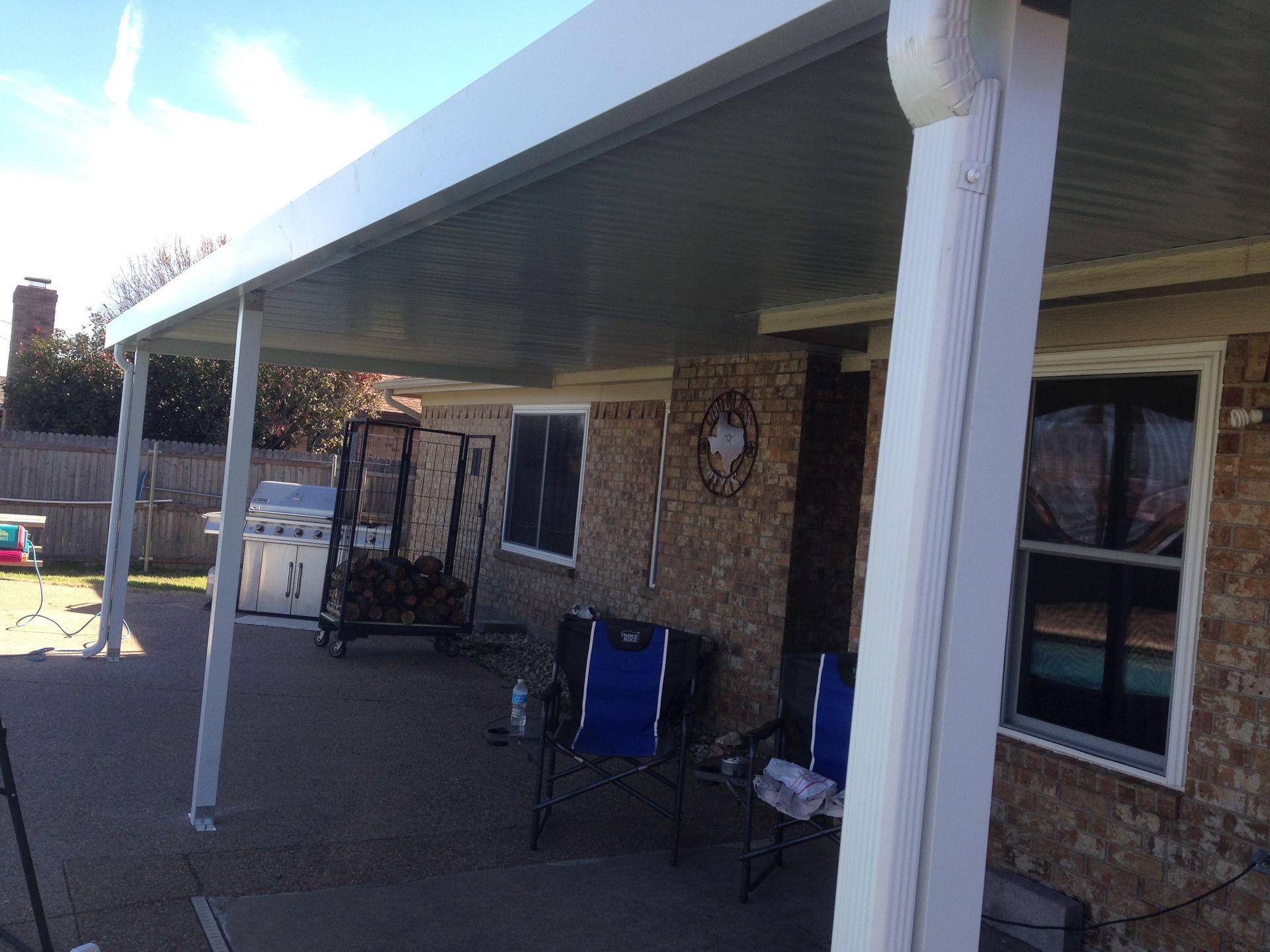 There is a covered patio with chairs and a swing in front of a house.