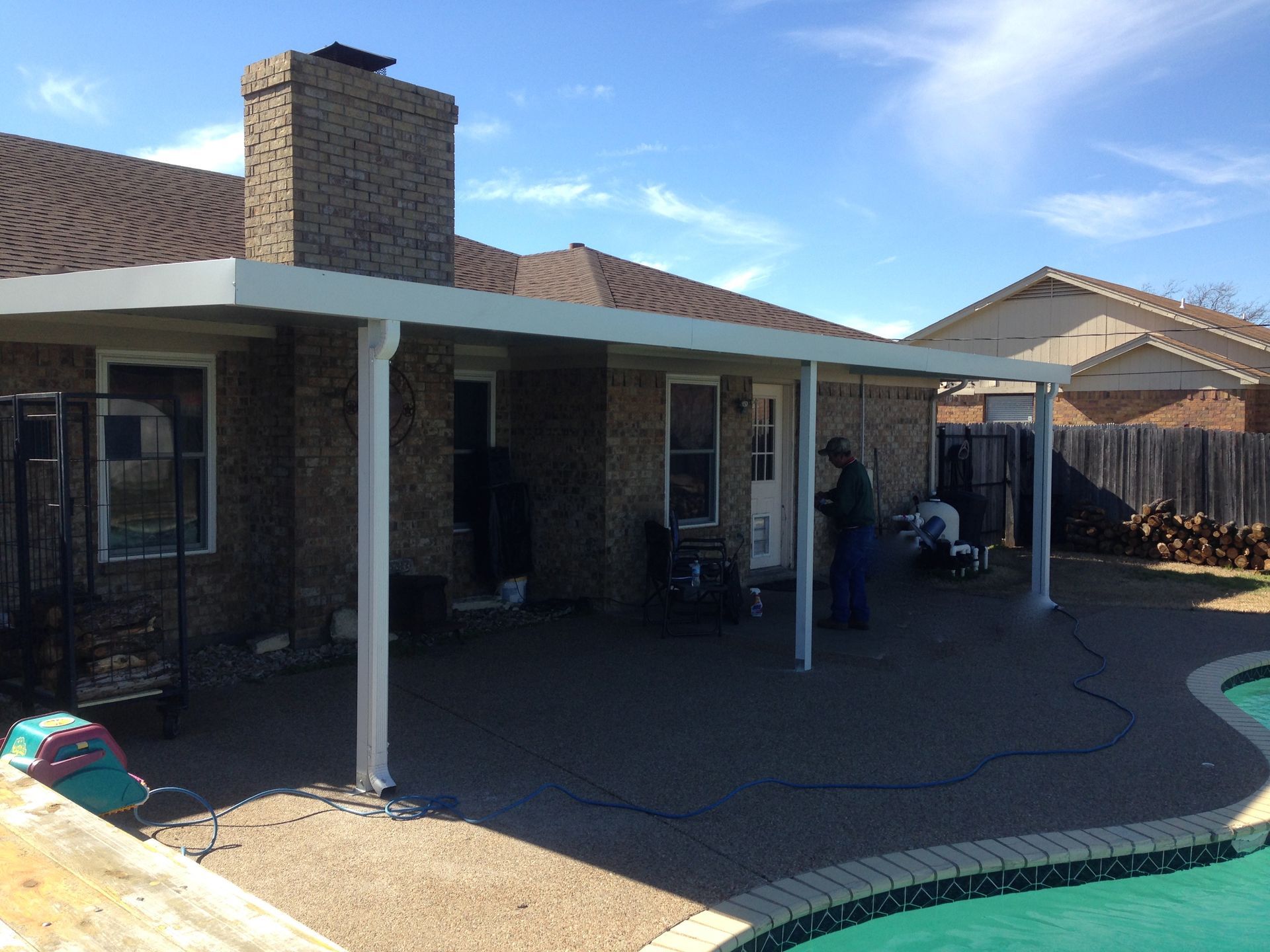 A man is standing under a patio cover next to a pool.