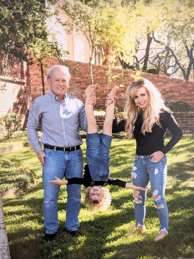 A man and woman are standing holding a child who is upside down