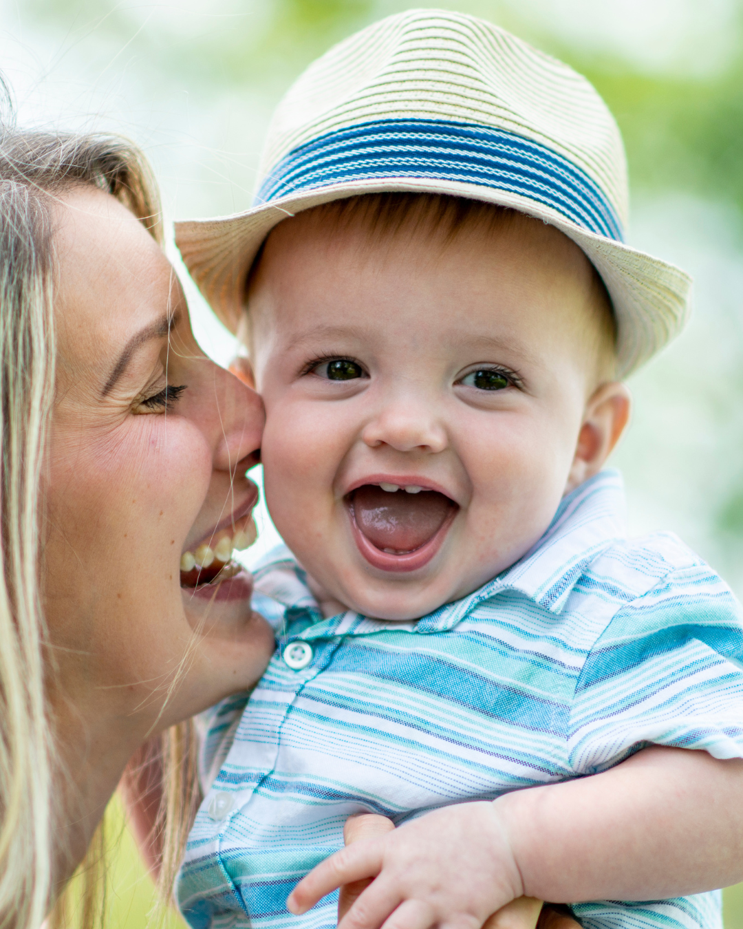 A woman is kissing a baby on the cheek while the baby is wearing a hat.