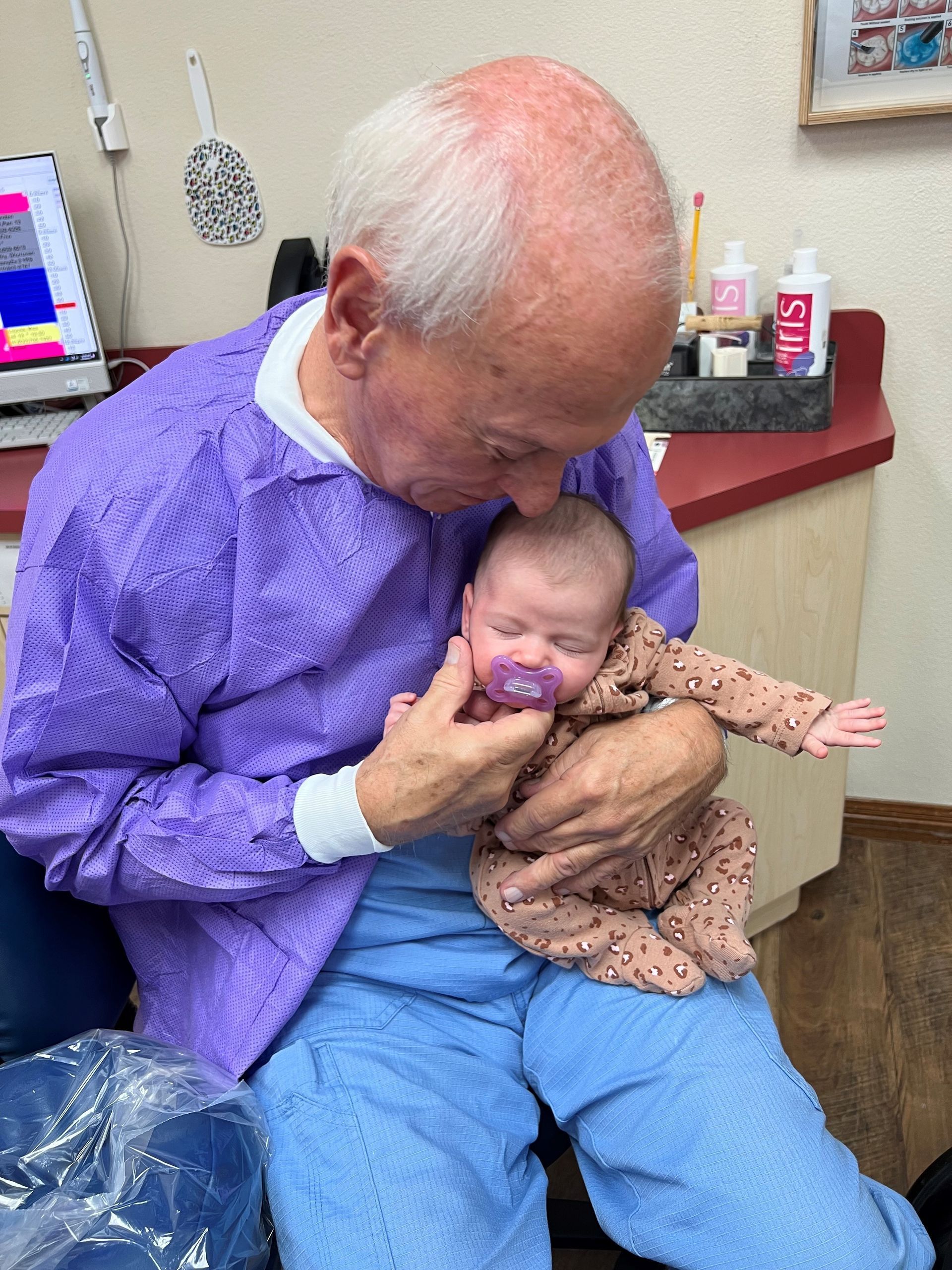 A man in a purple shirt is holding a baby in his lap.