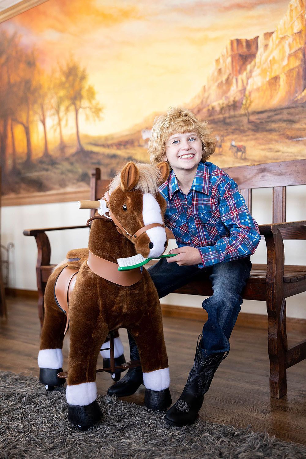A young boy is sitting on a bench next to a stuffed horse.