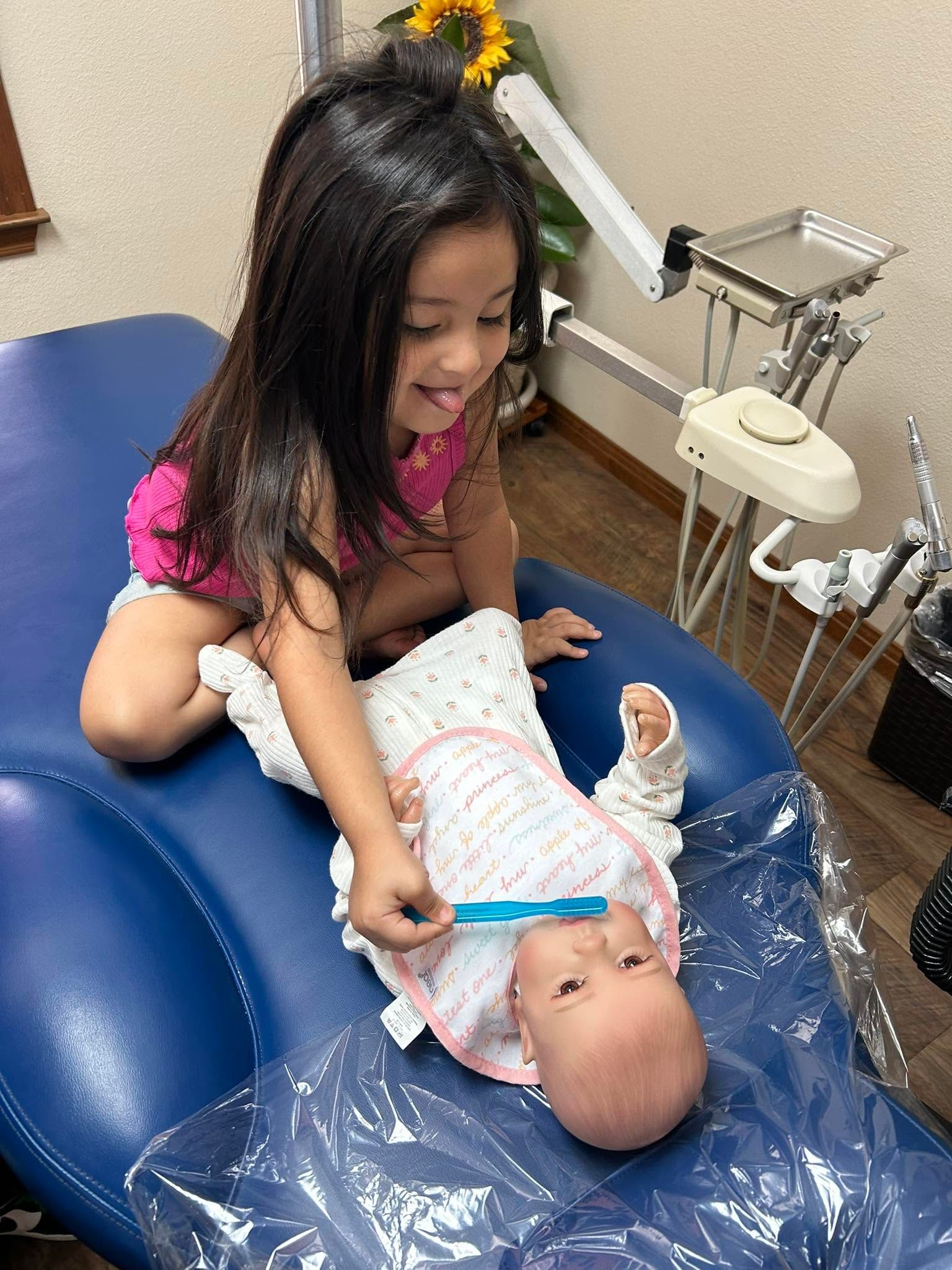 Girl in pink shirt smiling while holding a baby on a blue exam table in a clinic room