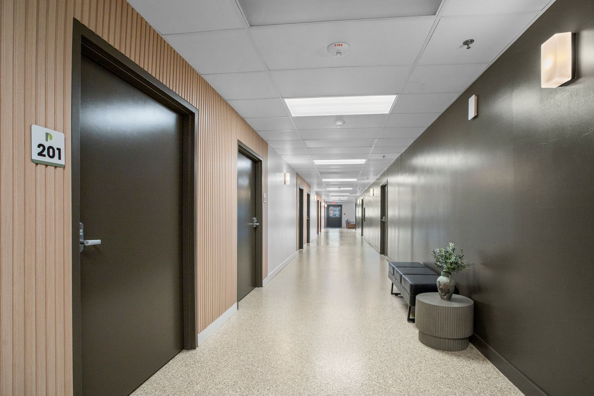 Long hallway with doors, beige speckled floor, brown walls, and recessed lighting.