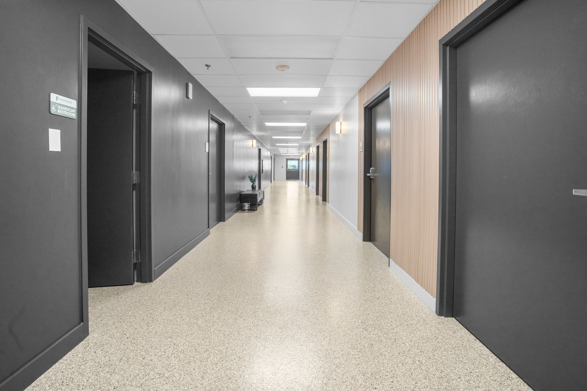 Long hallway in an office building with gray and wood panel walls and speckled floor.