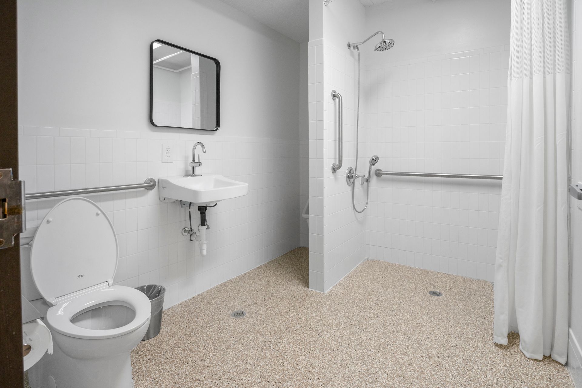 Accessible bathroom with toilet, sink, and walk-in shower with grab bars, white tiles, and terrazzo floor.