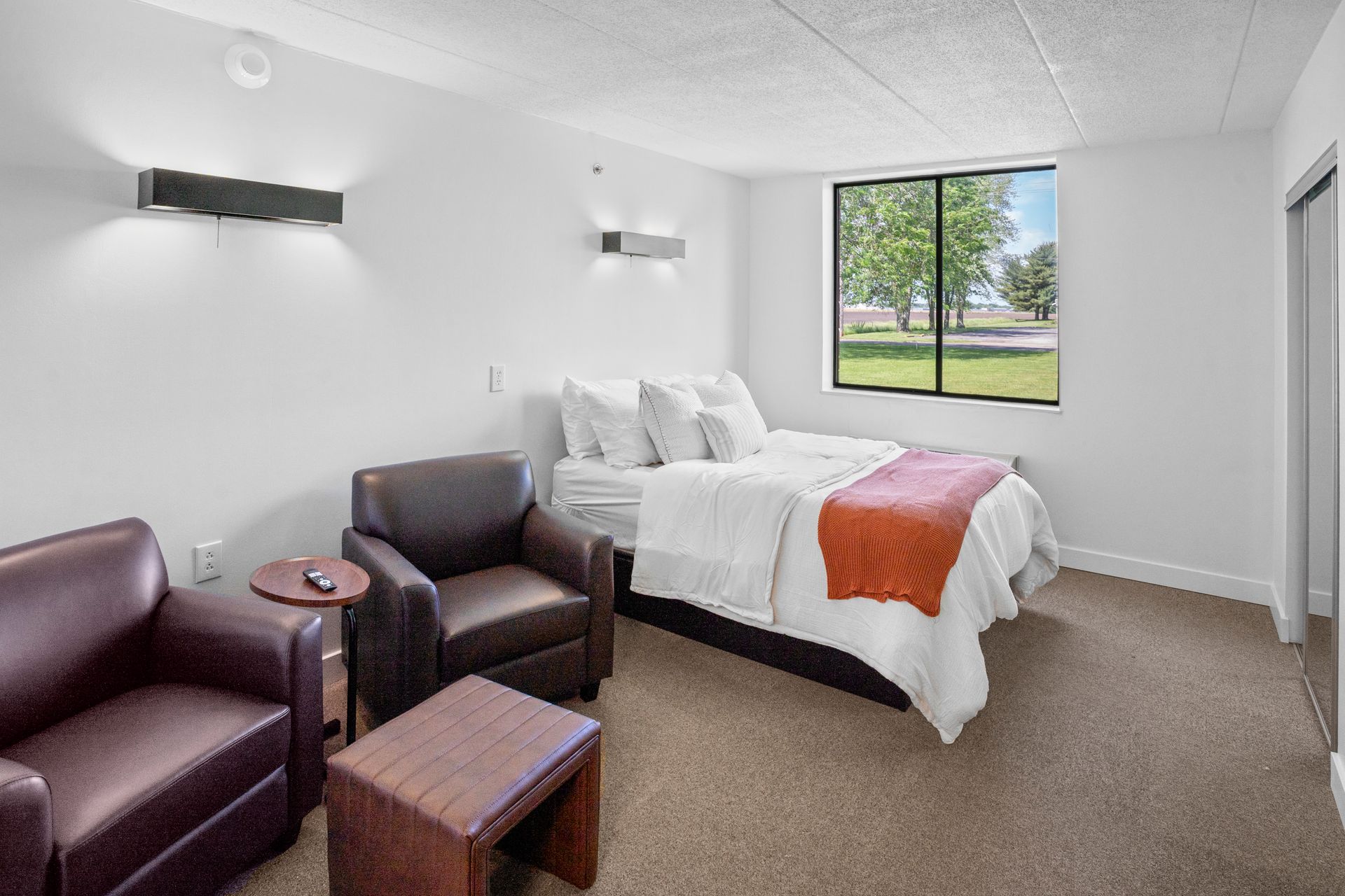 Bedroom with bed, chairs, window, and wall sconces.