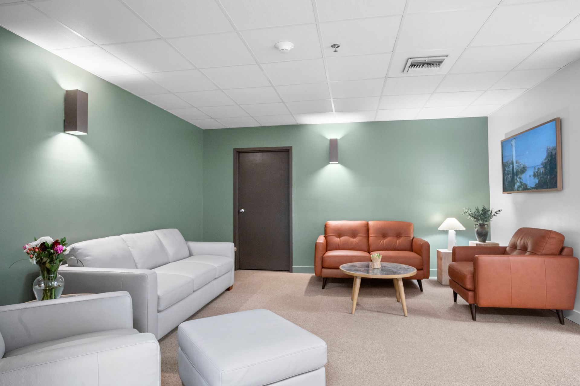 A waiting room with sofas, chairs, and an ottoman. Green walls and brown door.
