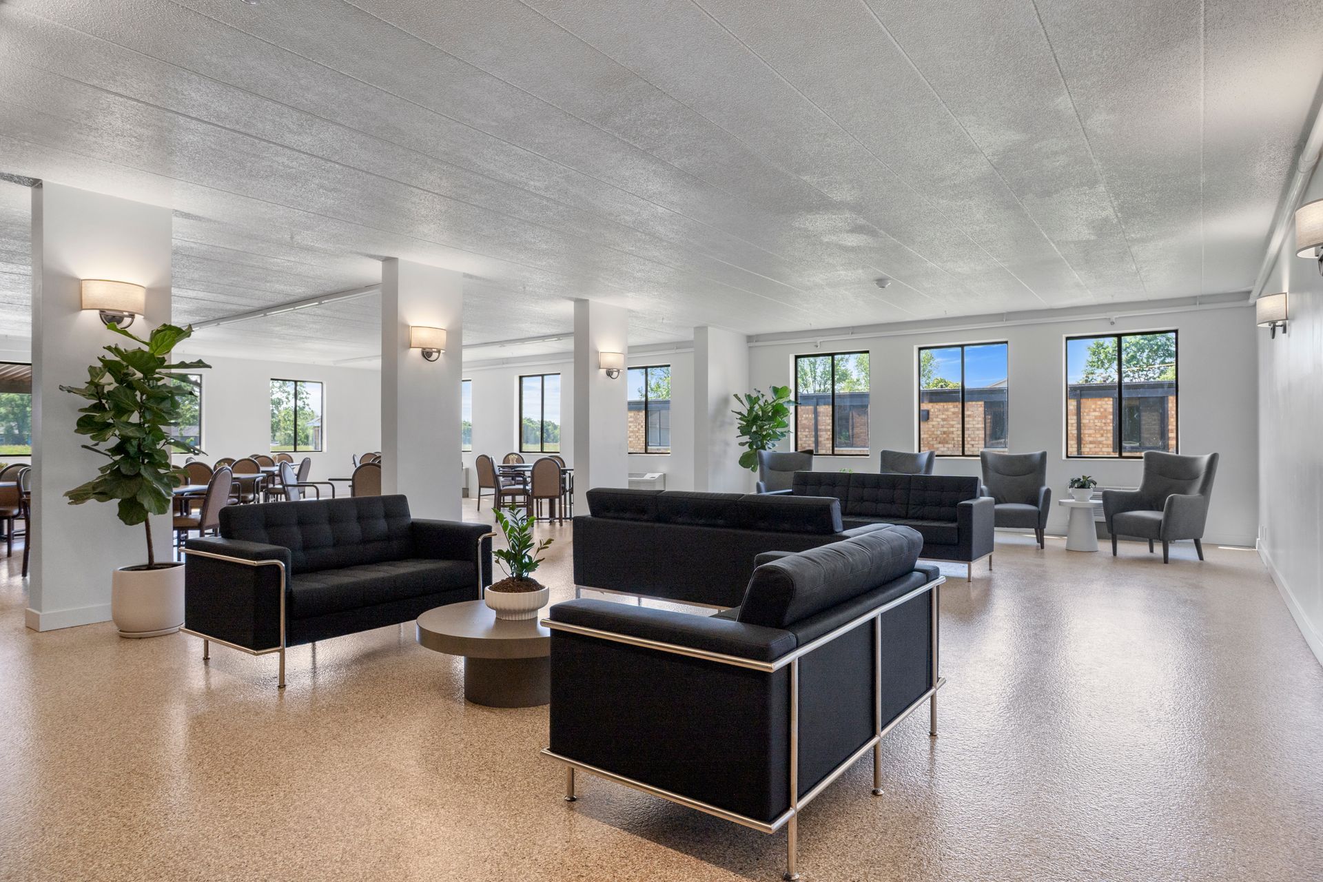 Spacious, modern lounge with black couches, a round coffee table, and large windows; neutral tones.