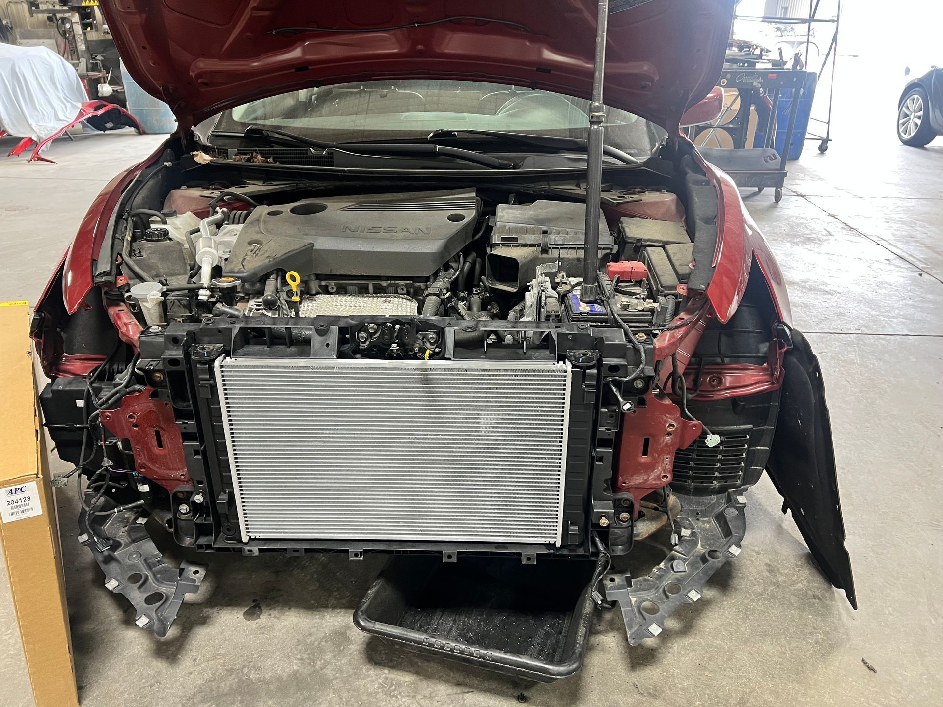 A red car with the hood up is being worked on in a garage.