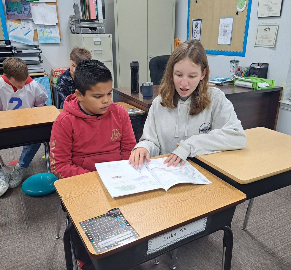 Person writing with a pencil on a desk in a classroom.
