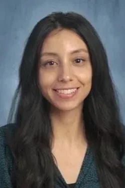Woman with long dark hair smiles at the camera, wearing a dark blue top, against a blue background.