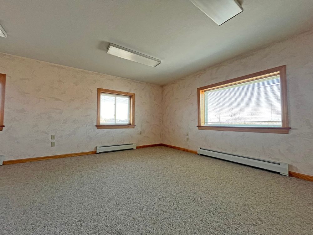 An empty room with a carpeted floor and two windows