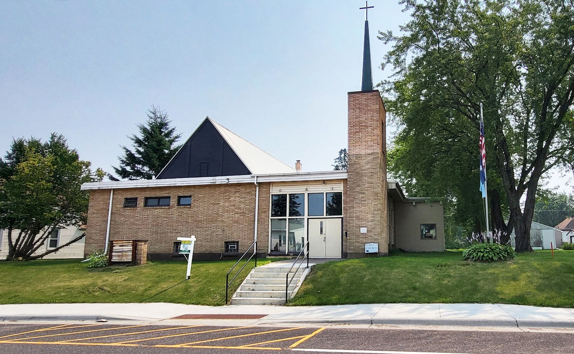 A brick church with a tall steeple and a black, angled roof. A stairway leads to the entrance with a lawn in front.