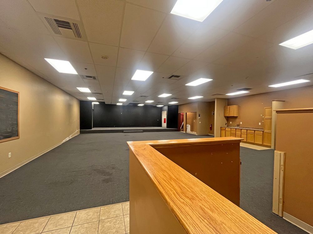 Empty, open-plan room with a dark stage, beige walls, and dark gray carpet.