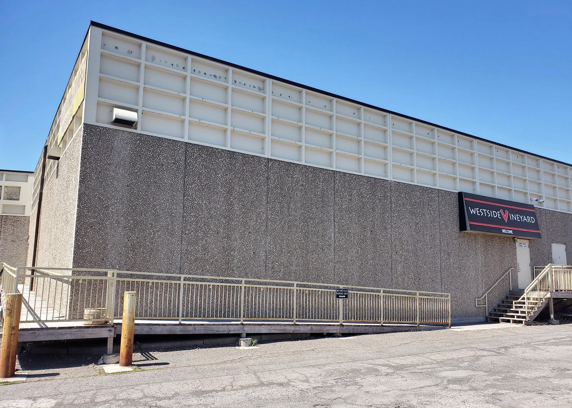 Building with textured gray stone walls and upper concrete panels. Ramp and doorway on right. 
