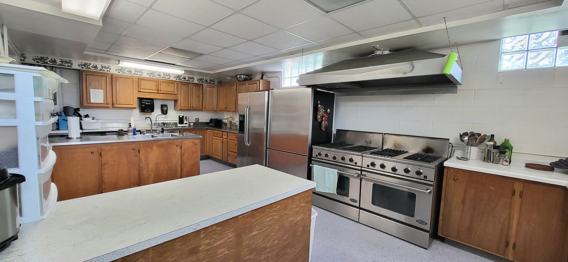 A commercial kitchen with stainless steel appliances, including a large stove and a refrigerator, wooden cabinets, and a central work island.