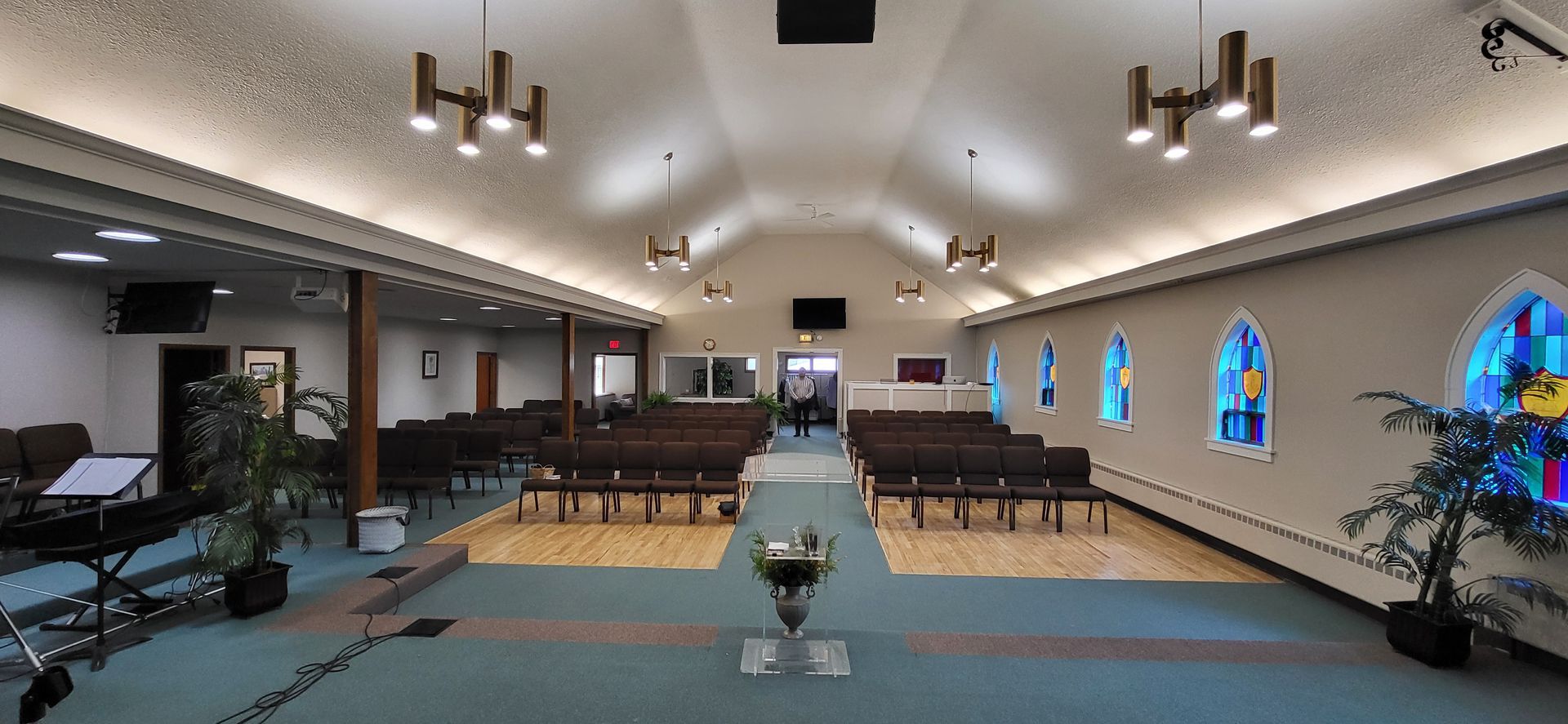 Interior view of a church sanctuary with rows of pews, stained glass windows, and decorative lighting.