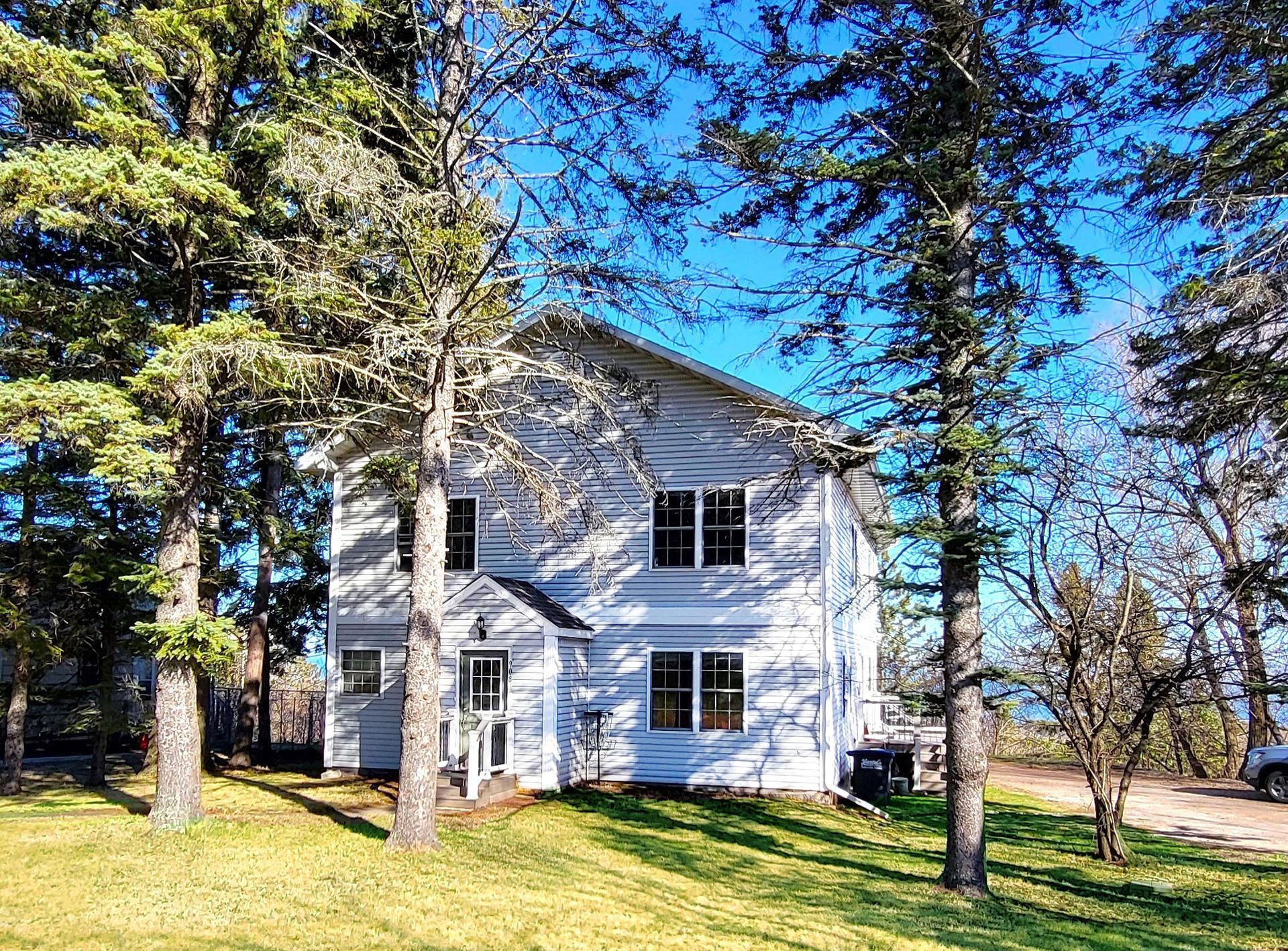 White two-story house with many windows, surrounded by trees on a sunny day.