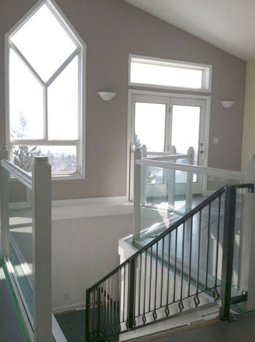 Interior view: staircase with glass and black metal railing, leading to a bright landing with windows and doors.