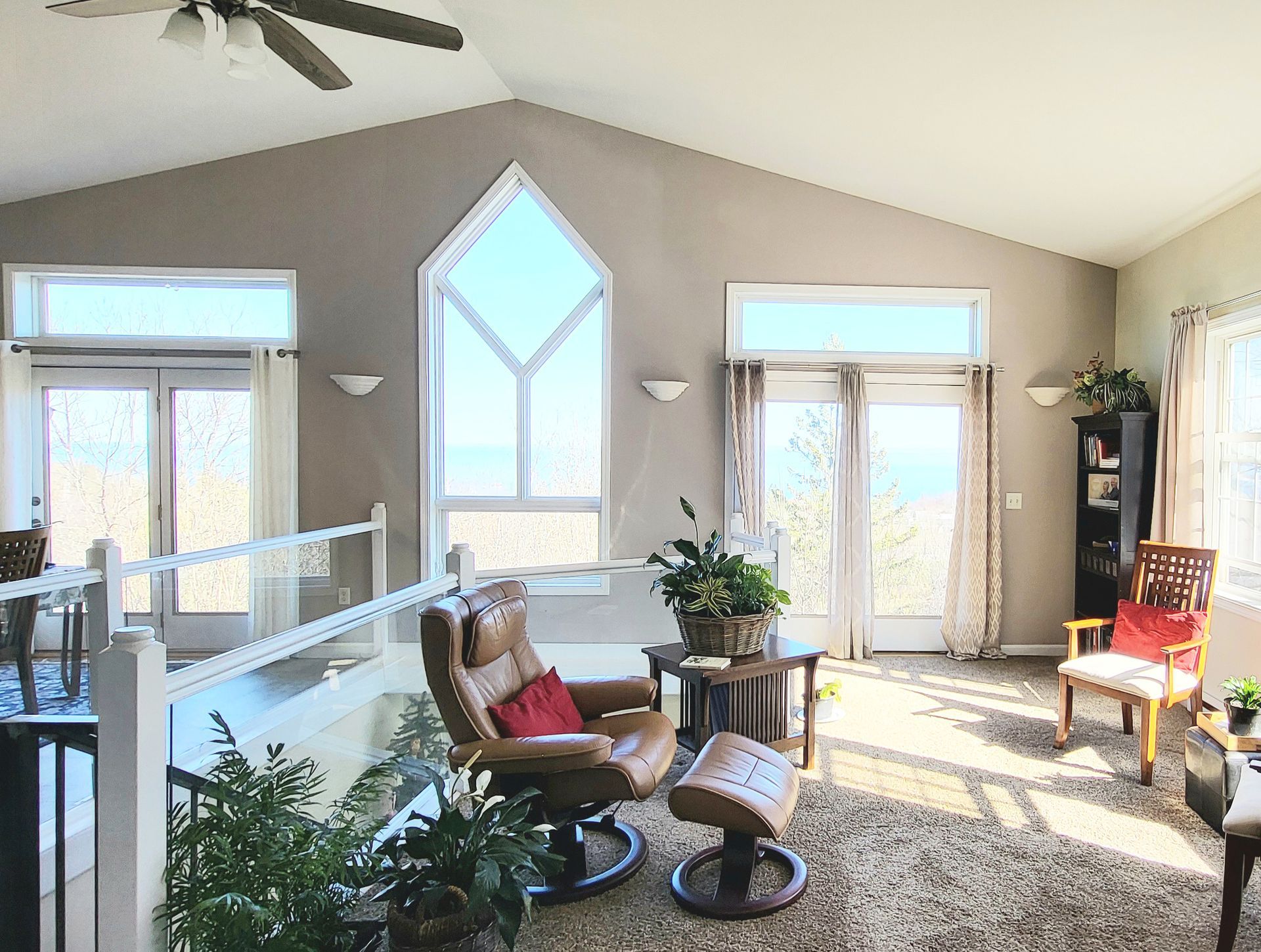 Bright living area with tall windows, leather chair, and plants; overlooking a view.