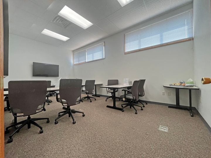 A conference room with tables and chairs and a flat screen tv.