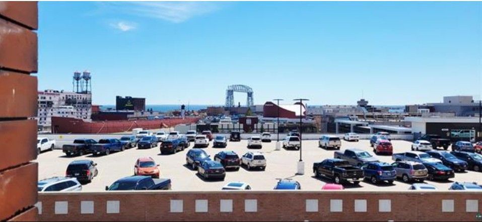 Wide view of a parking lot with many cars under a bright blue sky, seen from behind a brick wall