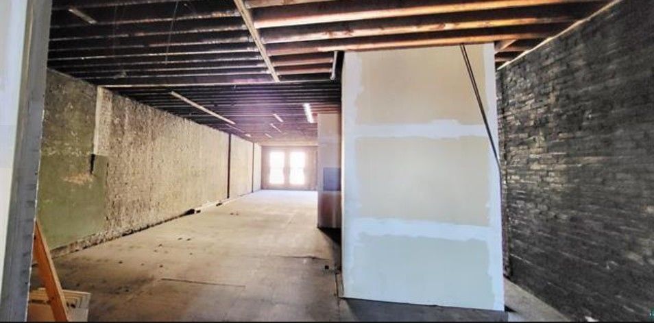 Dim unfinished interior with exposed beams, concrete floor, and a white partition wall near a bright doorway.
