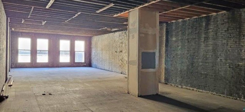 Empty unfinished room with exposed ceiling, concrete floor, and windows along one wall