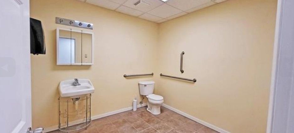 Accessible bathroom with sink, mirror, toilet, and grab bars on beige walls