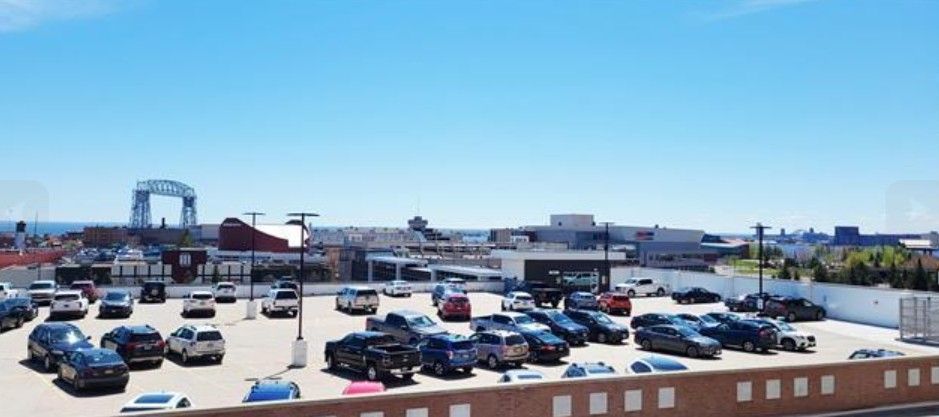 Aerial view of a crowded parking lot with many cars under a clear blue sky near industrial buildings