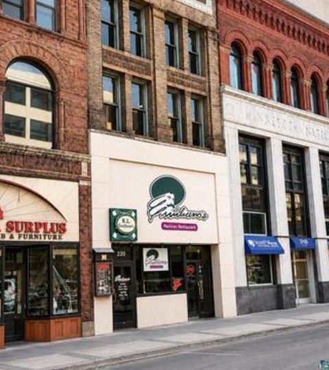 Street view of brick storefronts, including a white shopfront with a green sign and blue awnings nearby