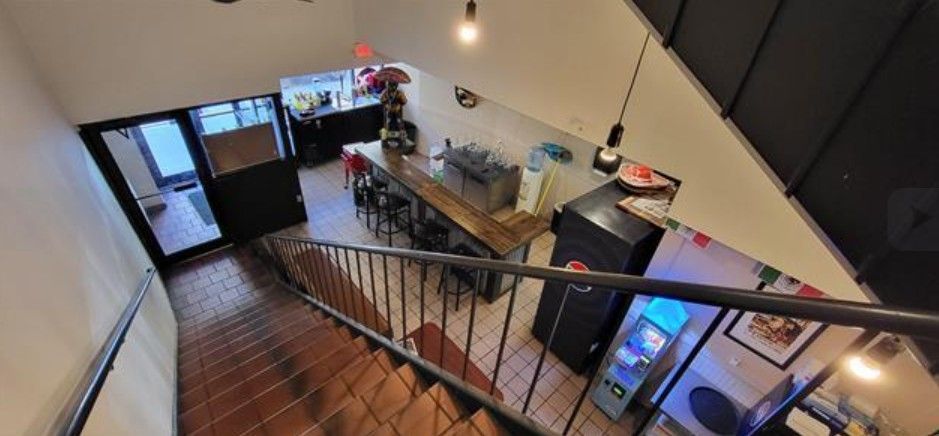 View down a staircase into a modern office lounge with tables, chairs, and a bright windowed entryway
