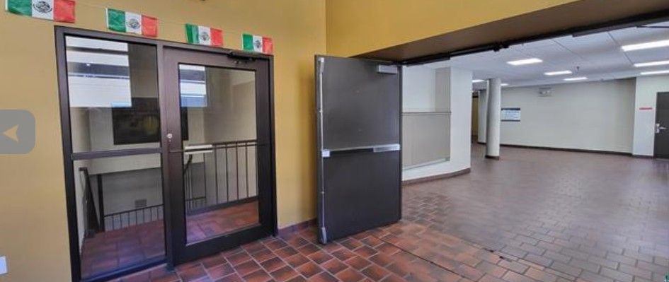 Open doorway to a tiled hallway and classroom, with glass entrance doors and colorful signs above.