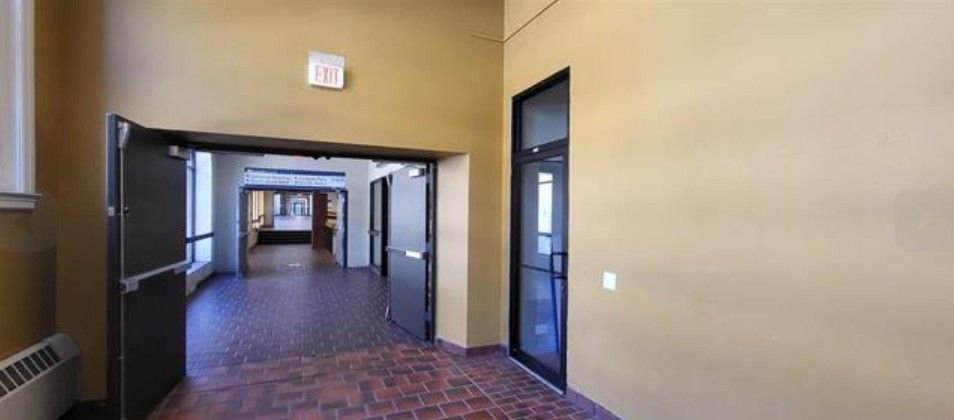 Empty hallway with beige walls, dark doorways, and red patterned carpet leading to a bright room