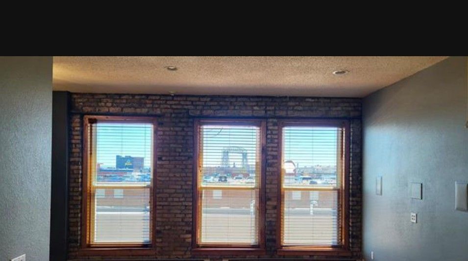 Empty room with three windows in a brick wall and gray walls, lit by daylight